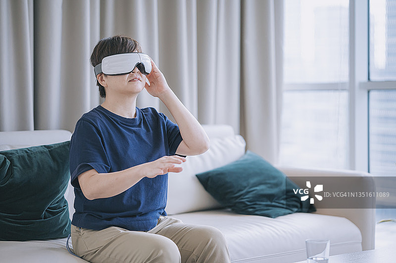 亚洲华人中年妇女使用虚拟现实模拟器在客厅坐在沙发上图片素材