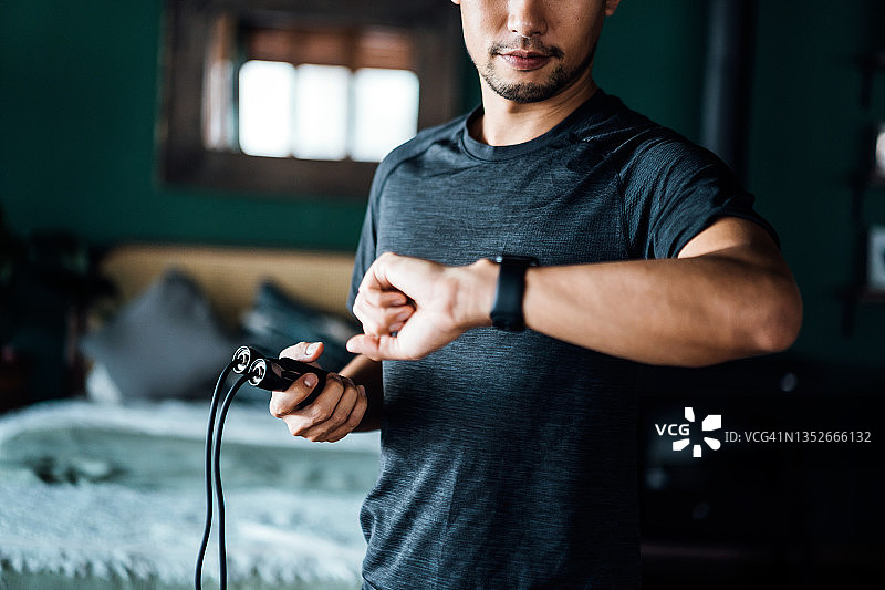 亚洲年轻男子在家锻炼的短照片，使用智能手表上的健身追踪器应用程序来监测训练进度和测量脉搏。保持身体健康健康、健身和科技的概念图片素材