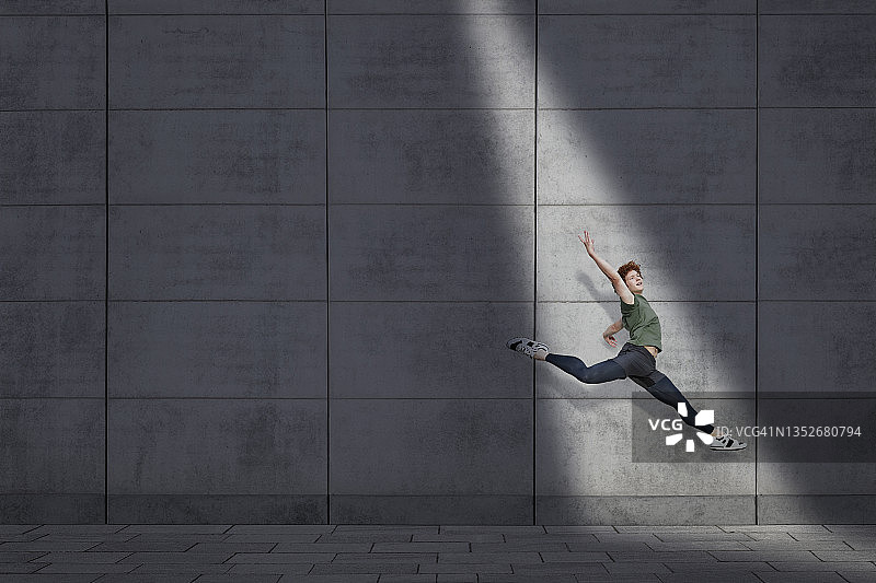 年轻的男子在灰色的墙壁上表演芭蕾舞图片素材