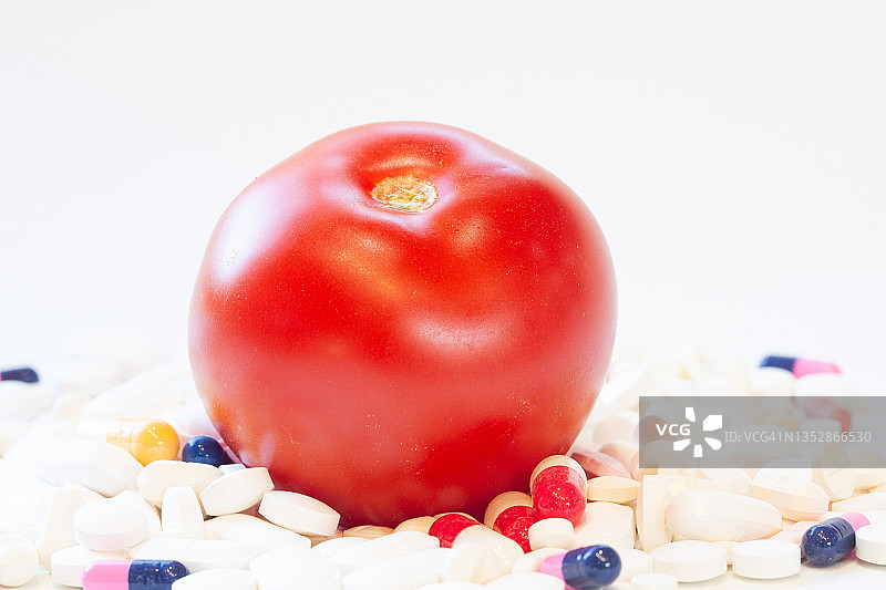 一个西红柿盖住一大堆药丸。维生素复合物的概念。图片素材