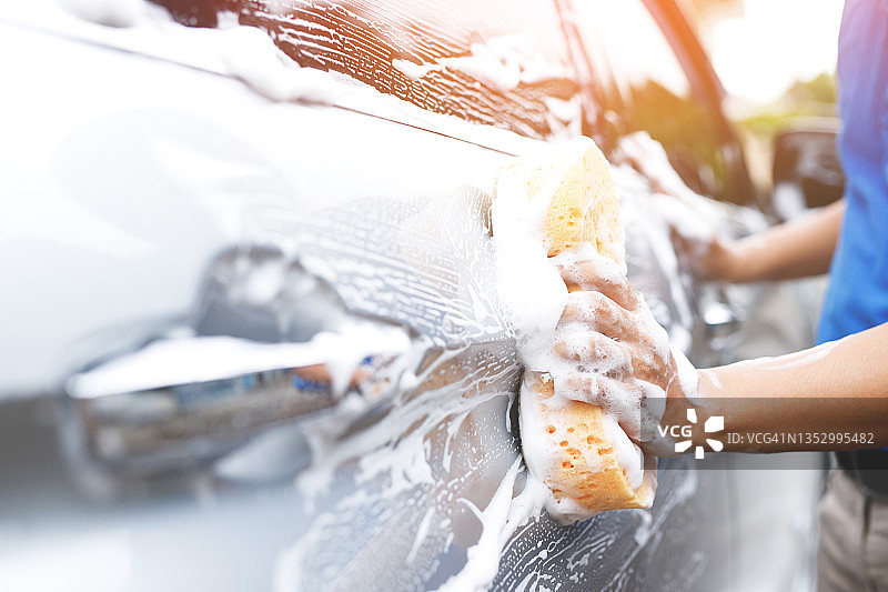人们用工人的手拿着黄色的海绵和泡沫洗刷窗来洗车。概念车清洗干净。留下写信息的空间。图片素材