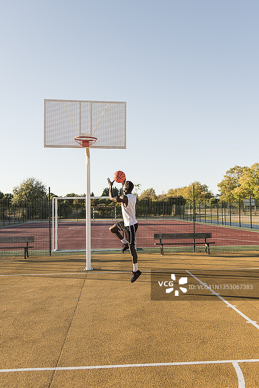 在公园的篮球场上，一个运动员跳得很高，扣篮。图片素材