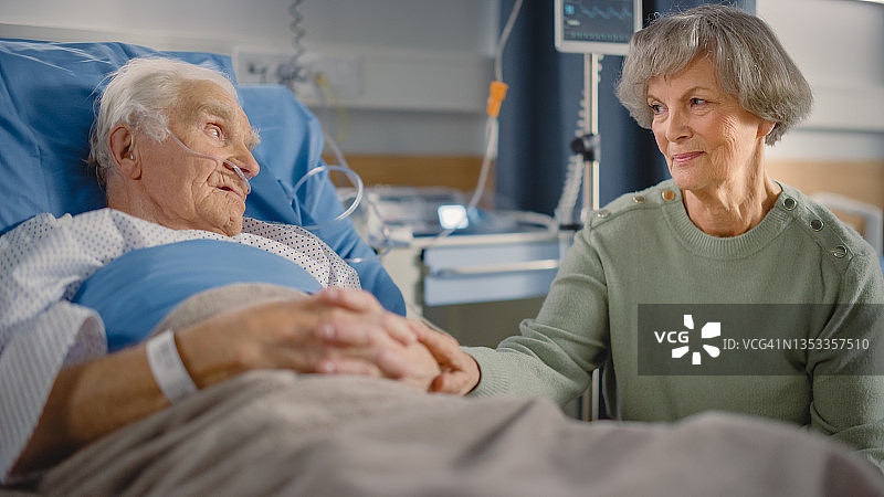 医院病房:老人躺在床上，他美丽体贴的妻子支持他坐在旁边，他们幸福地在一起谈论美好的时光。老人手术成功后完全康复图片素材