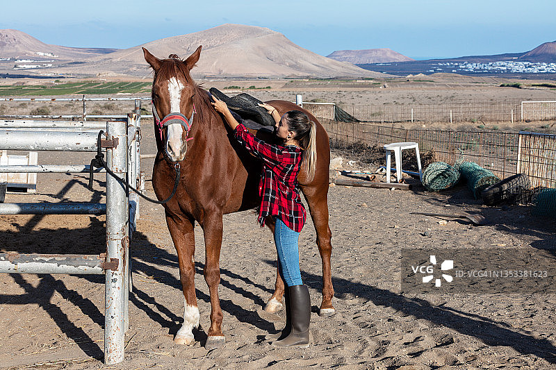 一名妇女在训练前给马套上马鞍图片素材