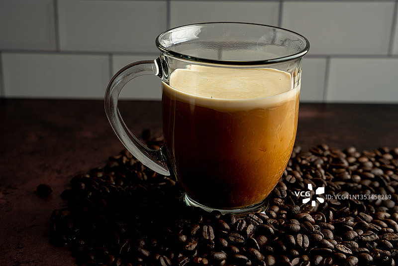 一杯新鲜的咖啡坐在整个咖啡豆中，奶油在咖啡中搅拌图片素材