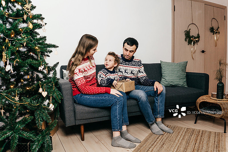 幸福的一家人坐在圣诞树旁的沙发上。图片素材