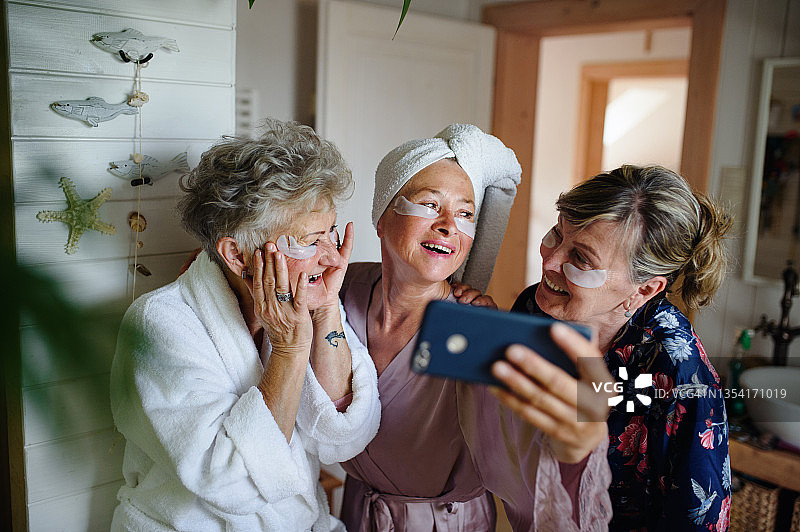 快乐的资深女性朋友们穿着浴袍在家自拍，自我护理的概念。图片素材