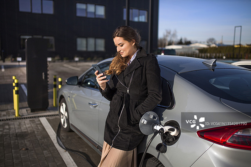 一个年轻女子在停车场给她的电动汽车充电图片素材