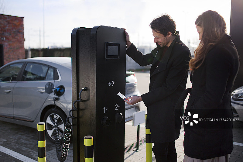 一对年轻夫妇在停车场用信用卡为他们的电动汽车充电图片素材