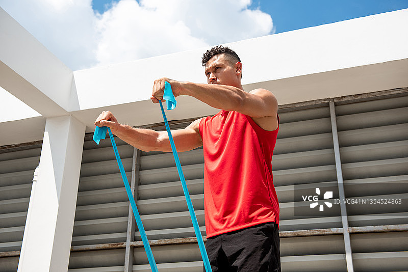 肖像的健康肌肉运动男子做前肩运动与阻力带在建筑屋顶图片素材