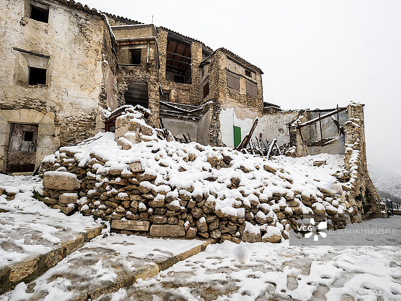 村庄的街道上有一座被雪覆盖的废弃房屋。图片素材