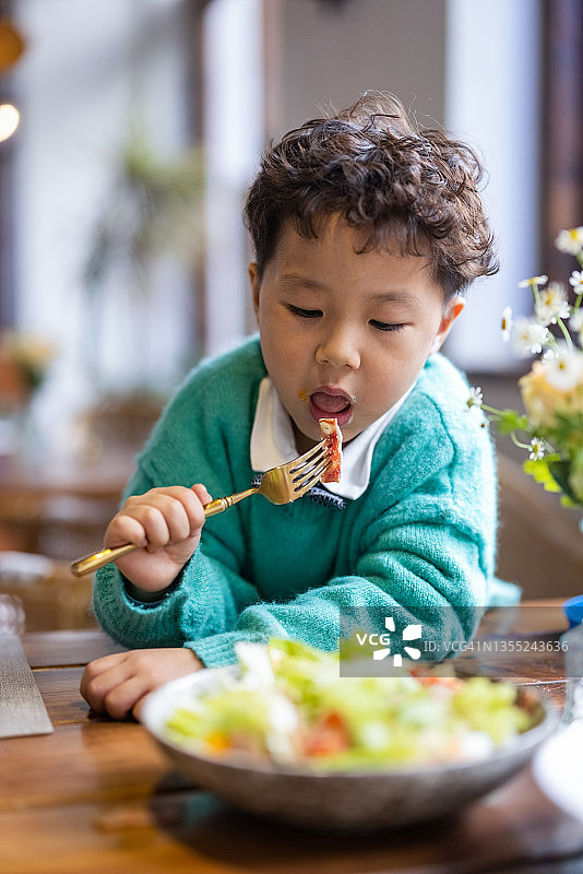 一个小男孩在餐馆里吃沙拉图片素材