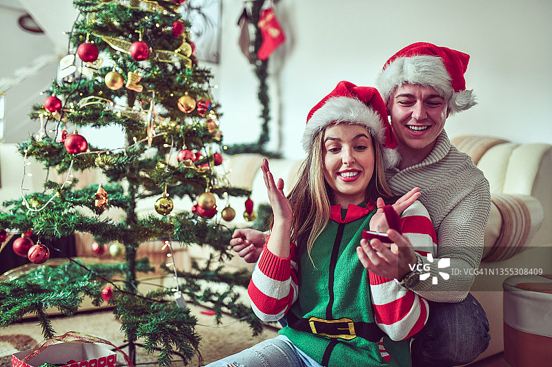 在一起装饰圣诞树的时候，微笑的女性得到了男朋友的求婚戒指图片素材