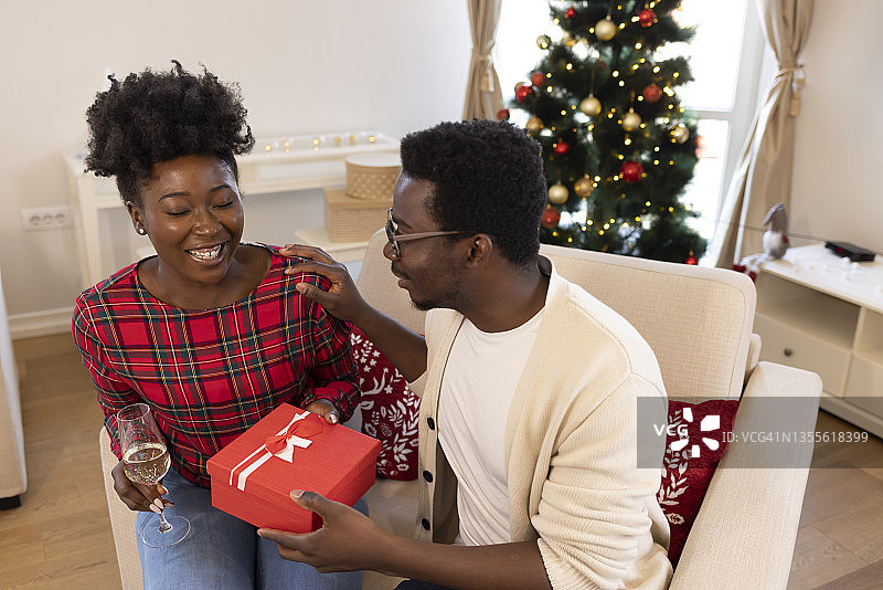 英俊浪漫的男人在给她可爱的圣诞礼物，贺卡概念后亲吻和拥抱情绪化的女人图片素材