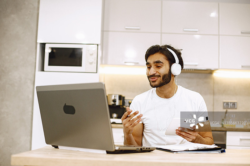 在线教育一个年轻的阿拉伯男子在家里用笔记本电脑学习并记笔记图片素材