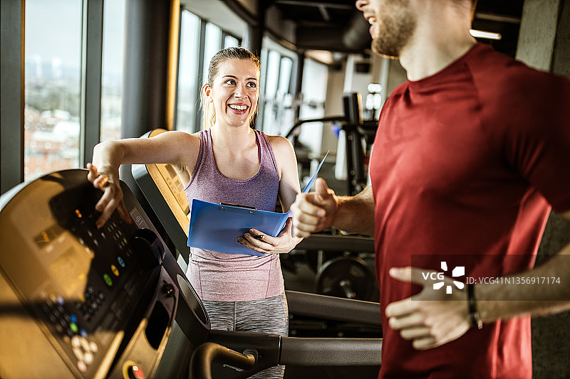快乐的女教练调整速度为男性运动员在跑步机上。图片素材