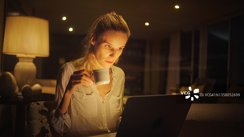 女商人在家工作到很晚。看着电脑屏幕，喝着咖啡图片素材