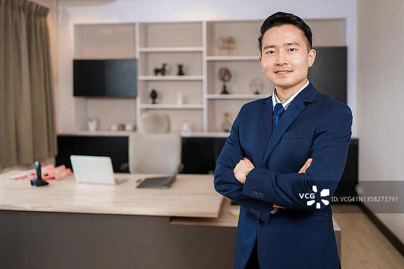 笑容满面的成功亚洲商人肖像在正式西装站在现代办公室摆姿势。图片素材