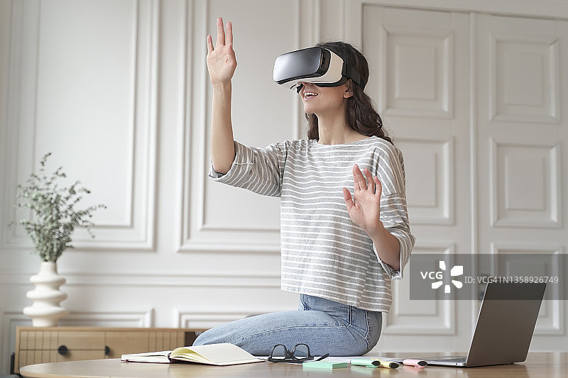 年轻的女员工戴着VR头盔护目镜，试图触摸虚拟现实中的东西图片素材