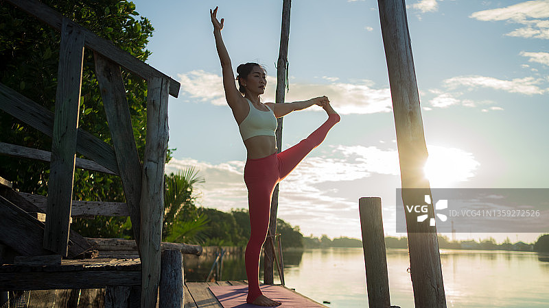 亚洲女人练习瑜伽在码头对天空。图片素材