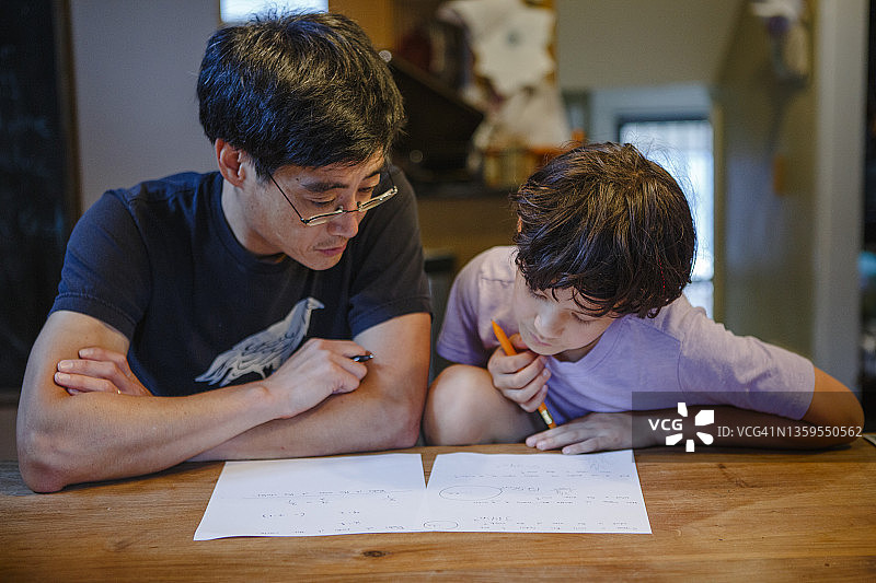 一个男孩和他的父亲一起坐在厨房的桌子前做作业图片素材
