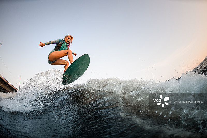 精力充沛的女冲浪手熟练地跳上冲浪板，顺着河波顺流而下图片素材