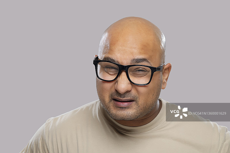 一个戴着眼镜的秃顶男人的肖像，在朴素的背景下露出困惑的表情。图片素材