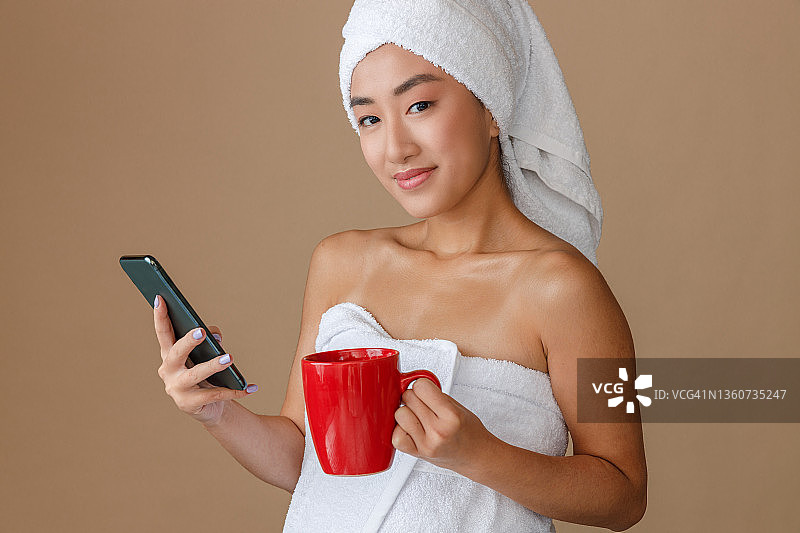 亚洲女性使用智能手机，洗澡后喝咖啡图片素材