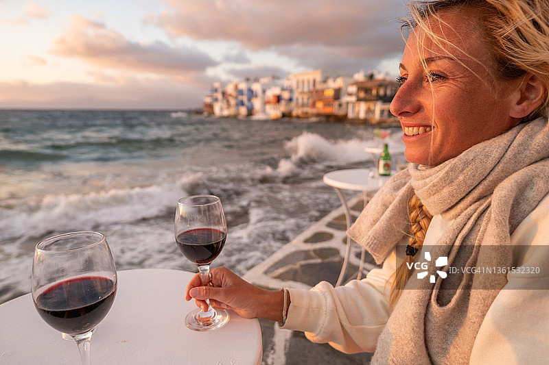 日落时分，一位年轻女子在海边喝红葡萄酒图片素材