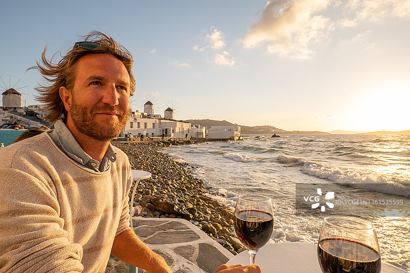 日落时分，一个年轻人在海边喝红葡萄酒图片素材