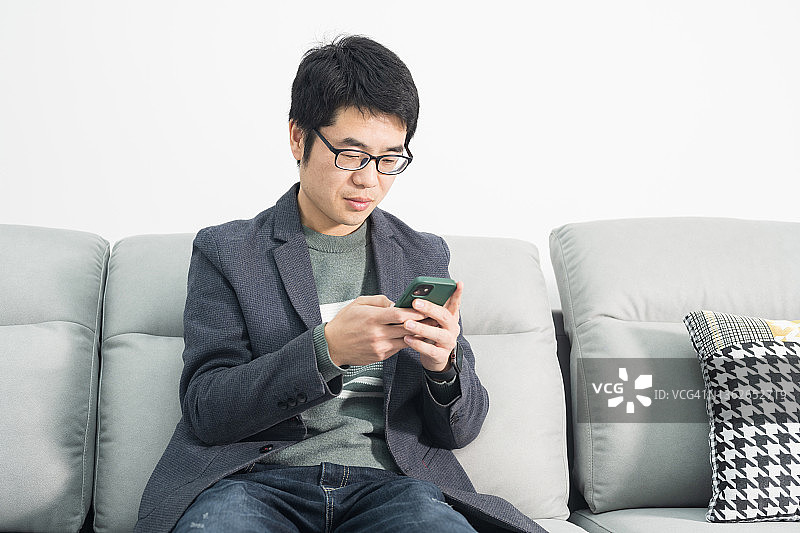 一名亚洲男子坐在客厅的沙发上玩手机图片素材