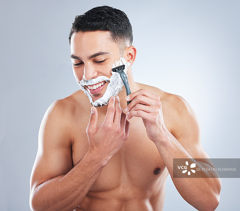 一个英俊的年轻人在灰色的背景下刮胡子图片素材