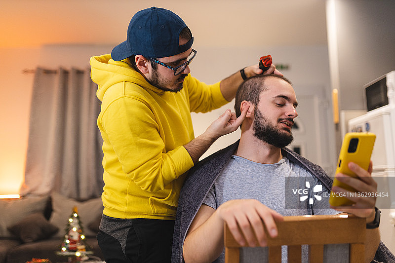 年轻的理发师向他的客户展示，由于疫情，他将如何在家里剪头发图片素材
