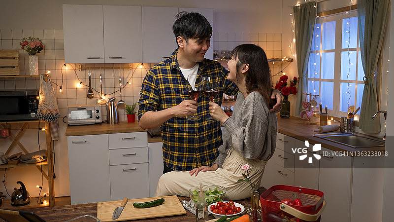 年轻的亚洲情侣在浪漫的关系调情，喝香槟，晚上在家里约会，有情人节的灯光装饰图片素材