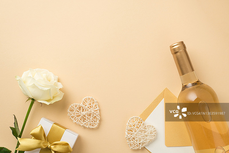 俯视图照片白玫瑰瓶白葡萄酒装饰藤心信封纸和白色礼盒与金色丝带蝴蝶结在孤立的米色背景与copyspace图片素材