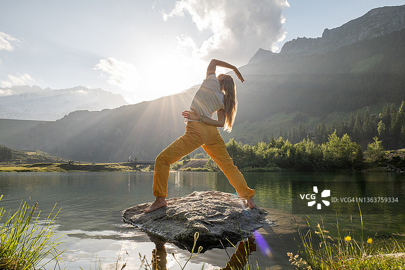 一名年轻女子在湖上的岩石上练习瑜伽图片素材