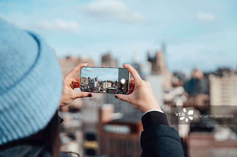 用智能手机拍摄城市风景的年轻女子。图片素材