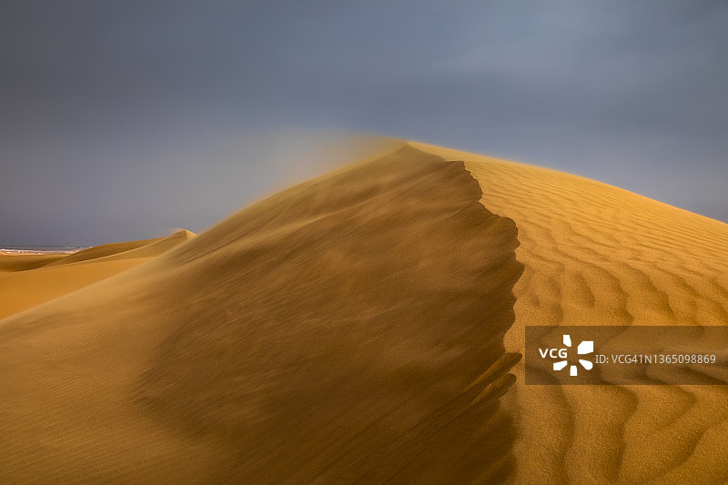 日落时的强风吹过沙漠中的沙丘。撒哈拉沙漠的沙尘暴图片素材