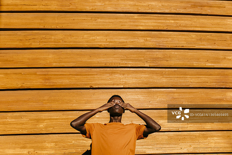 日落时分，一个男人双手蒙住眼睛站在橙色的墙前图片素材