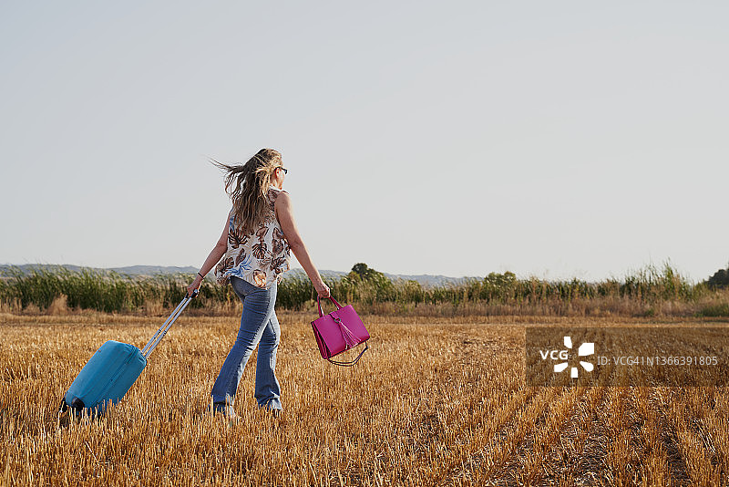 中年妇女拖着一个带轮子的小行李在草甸上行走。旅游的概念图片素材