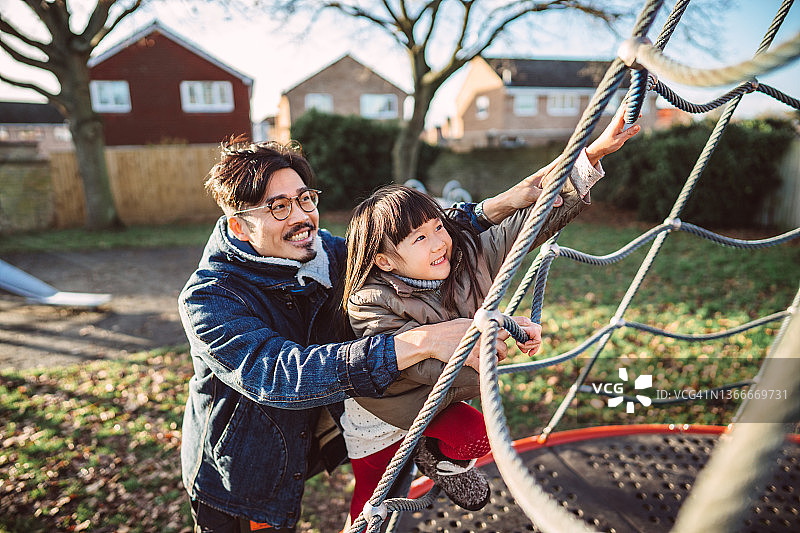 爸爸和女儿在公园里开心地玩着攀爬网图片素材