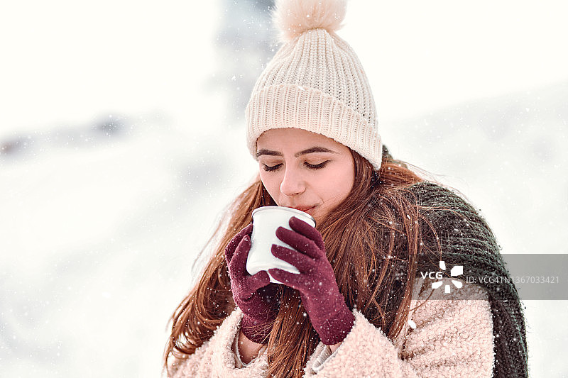 美丽的女性与雪帽享受温暖的咖啡在山雪图片素材