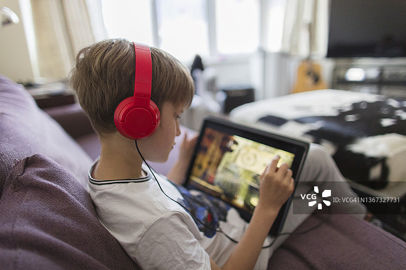 男孩戴着耳机，坐在沙发上玩电子游戏图片素材