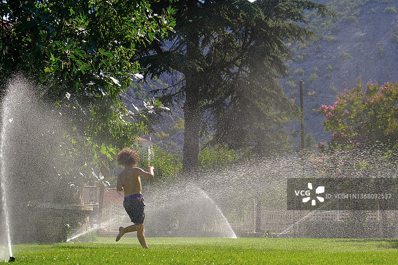 水的乐趣。在后院用草坪洒水器玩耍的孩子们。图片素材