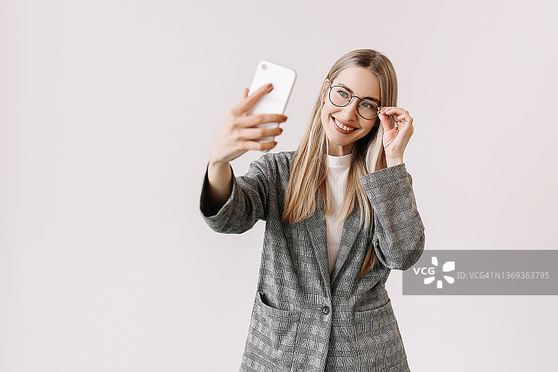 一名戴着眼镜、穿着休闲服装、面带微笑的女学生博主在一个白色孤立的背景下用智能手机自拍，并在Instagram上记录下了一个故事。一个成功的女商人通过视频聊天交流。文本的地方图片素材