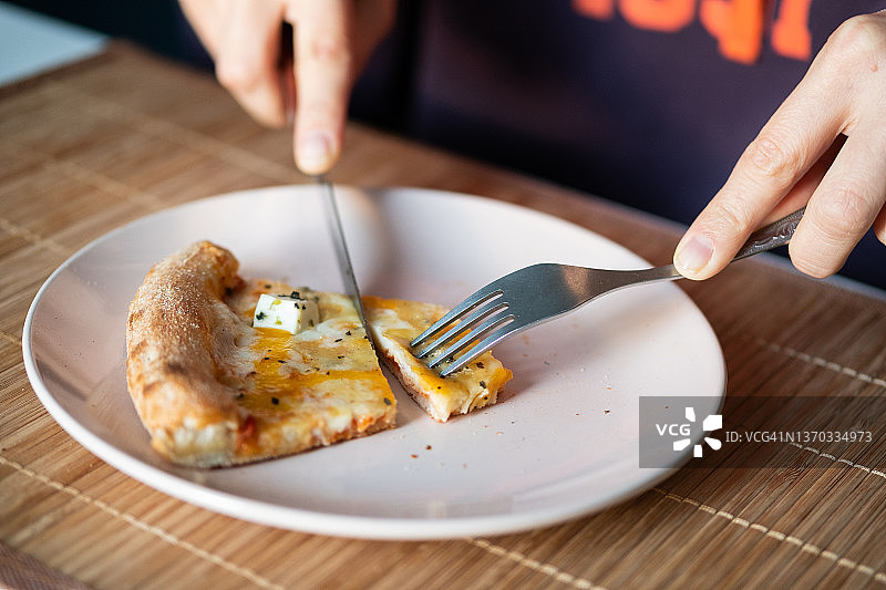 意大利披萨在陶瓷盘子里，在家里或咖啡馆的桌子上。一个女人切了一片披萨吃。玛格丽塔披萨加奶酪，切片，不带肉。素食的概念，快餐。送货到您的家或单位。图片素材