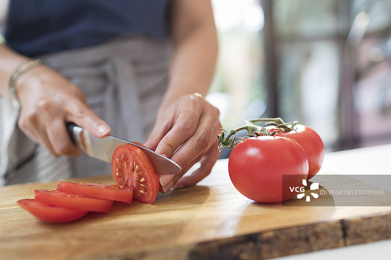近距离观察用刀在切菜板上切红番茄的女人图片素材
