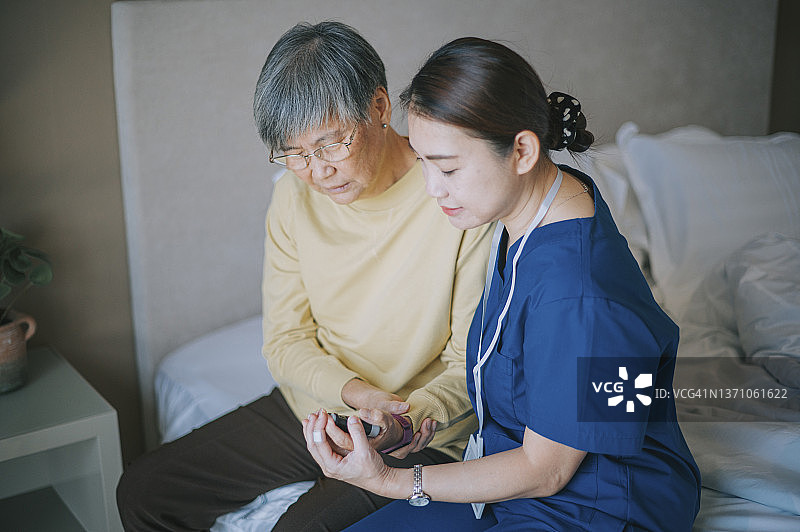 亚裔华人家庭护理员展示老年女性用手钳进行手腕锻炼，伸展手指，用手部扩张器挤压，物理治疗图片素材