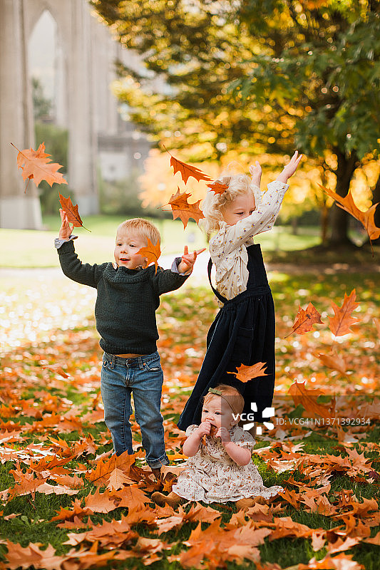 三个小孩一起在秋叶里玩耍图片素材
