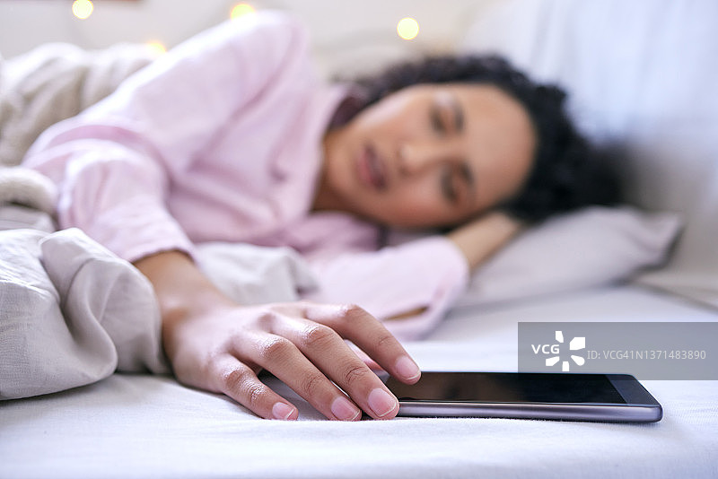 一张年轻女子躺在床上看手机的照片图片素材